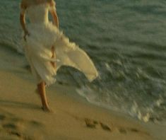 a woman in a white dress walking on the beach