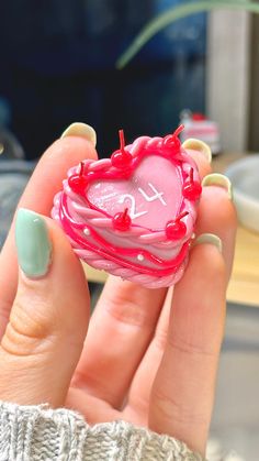 a hand holding a pink heart shaped object with writing on the front and bottom part