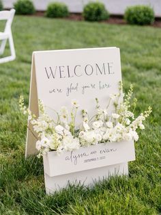 a welcome sign sitting in the grass with white flowers on it's back end