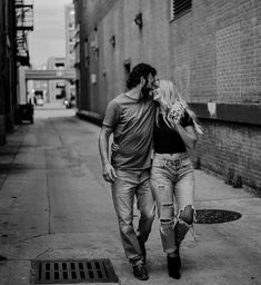 a man and woman are walking down the street in front of a brick building together