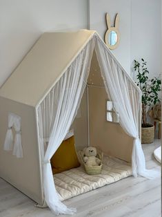 a tent bed with curtains and pillows on the floor in a room that has white walls