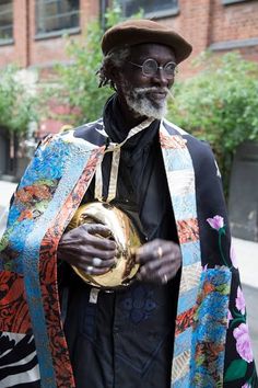 a man in an elaborately designed coat and hat holding a golden object while standing on the street