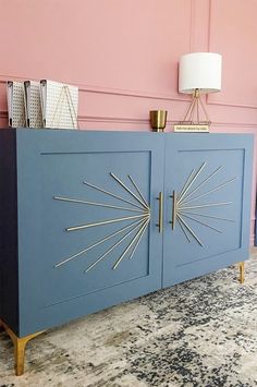 a blue cabinet with gold accents in a pink walled room next to a white lamp