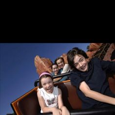 two girls and one boy are riding on a roller coaster at the amusement park together