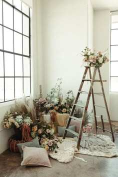 an arrangement of flowers and plants on the floor in front of a window with a ladder