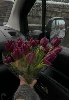 a person holding a bouquet of flowers in front of a car window with raindrops on the windows