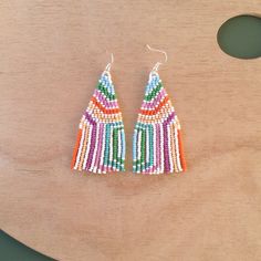 a pair of colorful beaded earrings sitting on top of a wooden table