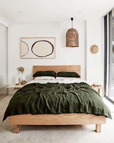 a bed with green sheets and pillows in a bedroom next to a large glass window