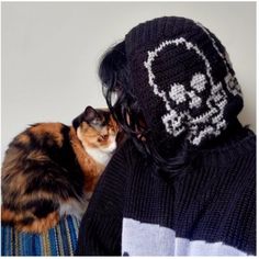 a cat sitting next to a person wearing a skull knitted hat