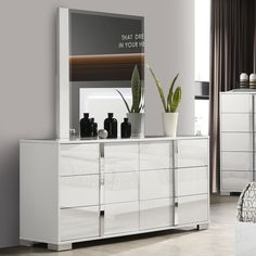 a white dresser sitting next to a bed with a plant on top of it in front of a mirror