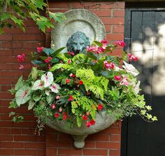 a planter filled with flowers next to a brick wall and black door handle on the side of a building