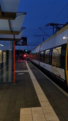 a train that is sitting on the tracks at night with its lights on and people walking by