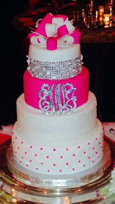 a three tiered wedding cake with pink and white frosting, decorated with monogrammed bows and bling