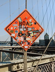 an orange road sign covered in stickers on the side of a bridge over water