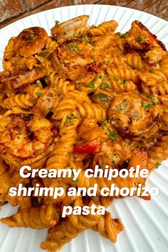 a white plate topped with pasta covered in shrimp and sauce next to a brick wall