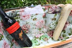 a bottle of wine and a hot dog in a flowered basket with utensils