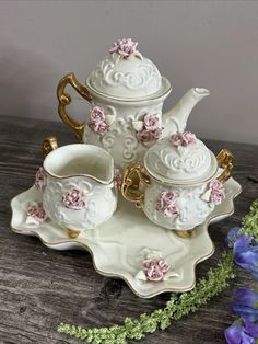 a white tea set with pink flowers and gold trimmings sits on a wooden table