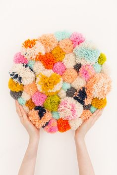 two hands are holding a multicolored knitted flower dishcloth in front of a white background