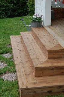 a wooden deck with steps leading up to a potted plant on the back porch