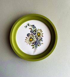 a plate with flowers painted on it sitting on a table next to a white wall