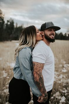 a man and woman standing in a field with their heads touching each other's noses