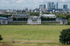 a large grassy field in front of some tall buildings with lots of trees and people walking around it