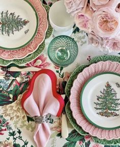 a table topped with plates covered in pink and green floral designs on top of a white table cloth