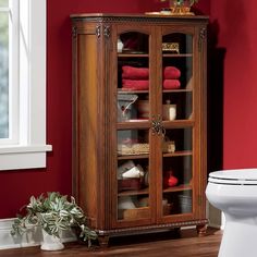 a bathroom with a toilet and wooden cabinet next to red walls in the corner,