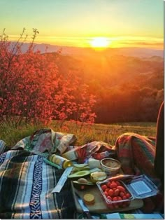 the sun is setting over a picnic with fruit and bread on it's blanket