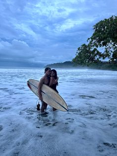 two people hugging each other while holding surfboards in the water at dusk on an ocean beach