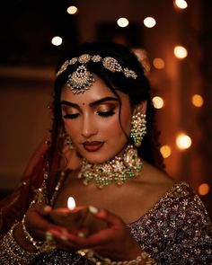 a woman in a bridal outfit holding a lit candle and looking at her phone