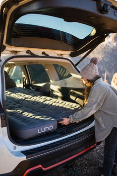 a woman unpacking an uno mattress in the back of a car with its trunk open