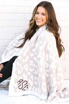 a woman is sitting on the bed wrapped up in a white and brown leopard print blanket