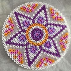 a circular object made out of beads on top of a white surface with an orange and purple design