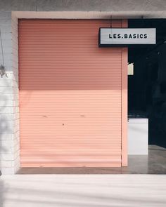 an orange roller up door in front of a brick building with the words les basics written on it