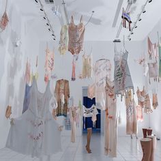 there are many clothes hanging from the ceiling in this room, and one person is walking down the hall