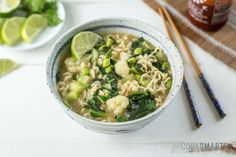 a white bowl filled with soup next to chopsticks and lime slices on a table