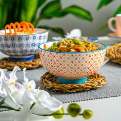 two bowls filled with food sitting on top of a table next to flowers and utensils