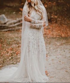 a woman wearing a wedding dress and veil standing in the woods with her arms crossed