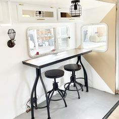 two stools sit in front of a long table with mirrors on the wall behind it