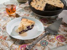 a piece of blueberry cheesecake on a plate next to a cup of tea