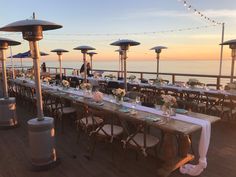 an outdoor dining area with tables and umbrellas on the deck overlooking the ocean at sunset