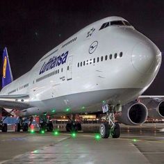 an airplane sitting on the tarmac at night with its lights on and people standing around it