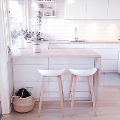 two white stools in front of a kitchen counter with plants on the top shelf