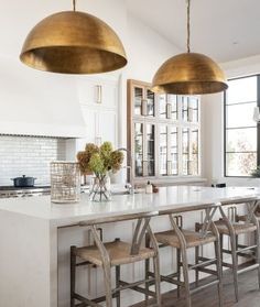 a kitchen with two pendant lights over the island and four stools in front of it