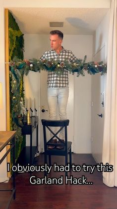 a man standing on top of a chair holding a christmas wreath over his head with the caption, i obviously had to try this garland hack