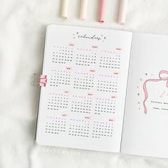 an open planner with pink and white markers next to it on top of a bed