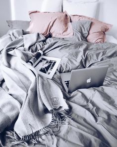 an apple laptop sitting on top of a bed covered in blankets and pillows with pink pillows