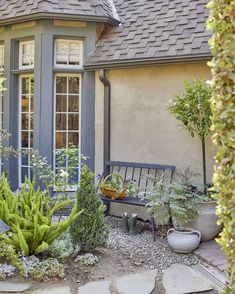 a bench sitting in front of a house next to a tree and plants on the ground