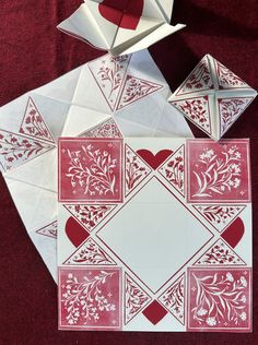 an origami heart and flower arrangement on a red tablecloth with white paper